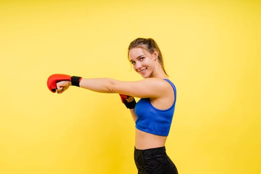 Woman boxer in gloves training on a grey and yellow background studio