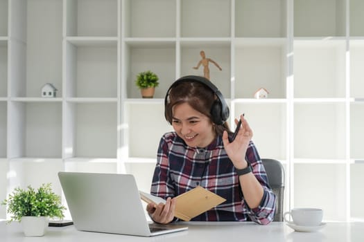 Young woman studying online from home, wearing headphones, using a laptop, and taking notes in a modern home office.