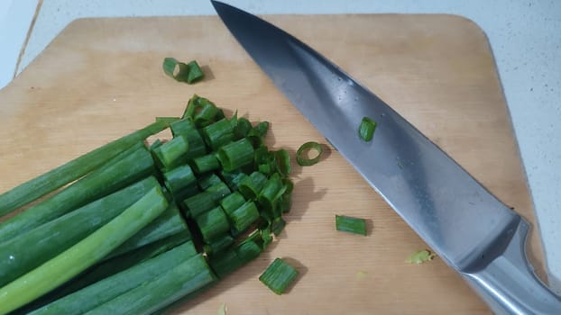 health food green fresh chopped onion, aluminum knife, background healthy cooking, wooden kitchen board. High quality photo