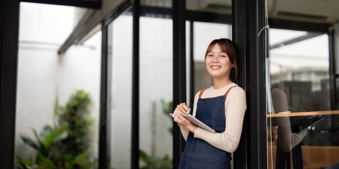 A young woman cafe owner stands at the entrance of her modern cafe, smiling and holding a notebook, embodying the entrepreneurial spirit of starting a small business.