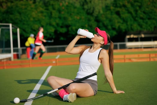 girl hockey player plays field hockey on a sunny day, hockey player drinks water during a break in the match, active sport for girls