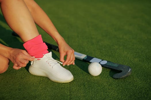 girl hockey player tying sneakers on the field hockey field, concept of playing field hockey, women's sport