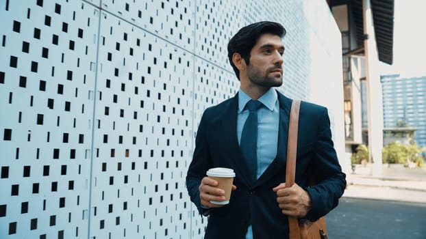 Skilled business man walking in suit outfit while holding coffee cup. Professional manager standing near architectural building. Going to working in morning, seeking for successful job. Exultant.