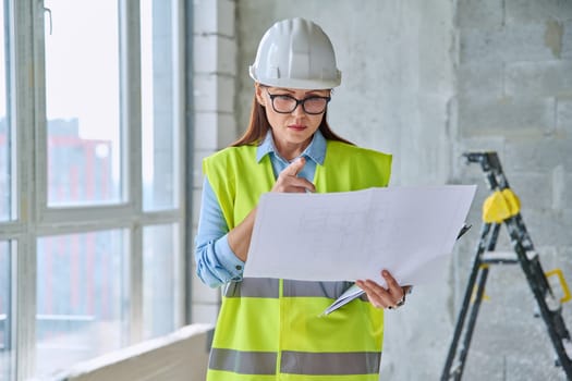 Technical profession woman in safety vest helmet working on construction. Confident serious industrial female engineer builder inspector supervisor architect with papers. Construction industry renovation