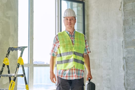 Portrait of male industrial worker builder engineer in safety helmet vest with suitcase of tools inside construction site. Construction repair renovation service development work concept