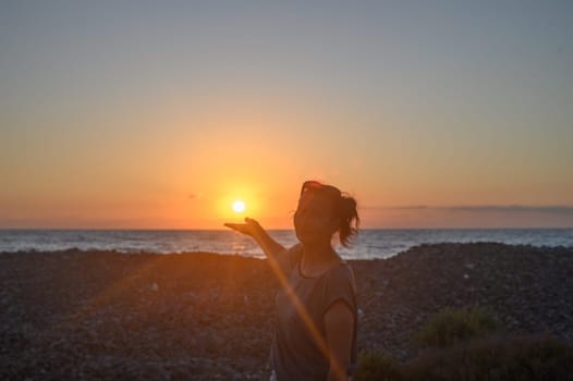 Silhouette of a young Caucasian woman holding the sun in her hands. On the seashore at sunset. 2