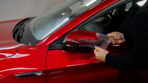 The master applies vinyl film to the side view mirror of a car