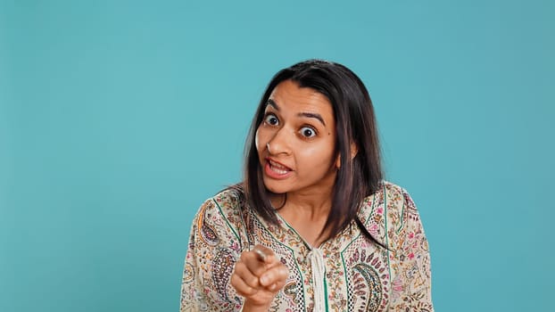 Upset indian person fighting with friend, doing scolding gesturing, isolated over studio backdrop. Annoyed woman arguing with opponent during discussion, doing admonishing hand gestures, camera B