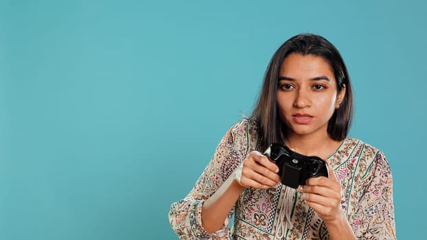 Cheerful woman playing videogames with controller, studio background. Indian gamer smiling, having fun by participating in PvP online multiplayer game using console system, camera B