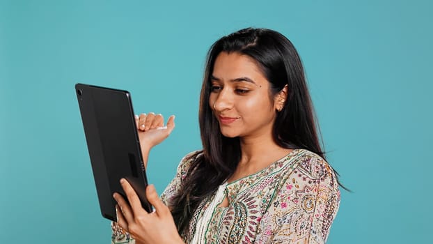 Upbeat woman having friendly conversations during teleconference meeting using tablet, studio background. Person having fun catching up with mates during online videocall on digital device, camera B
