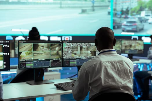 Observation room employee reviewing video surveillance footage to find illegal activity within urban traffic, big screen. African american man collecting data via CCTV radar system.