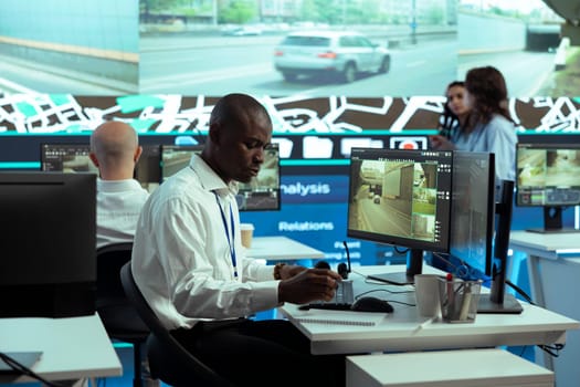 African american dispatcher monitoring express shipping activity through city traffic, following delivery trucks via gps tracking on satellite map. Young employee in call center helps with shipment.