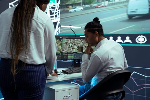 Indian employee consulting his african american team leader on cargo logistics insight, discussing about improving express shipment by using gps coordinates on satellite map, order tracking.