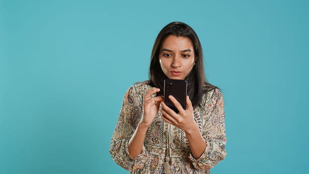 Woman scrolling on smartphone screen, doing online shopping, amazed by beautiful clothes. Portrait of relaxed person browsing internet websites, exclaiming in astonishment, studio background, camera A