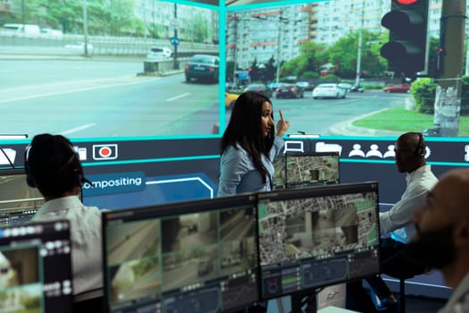 Indian woman team leader guides her staff to monitor surveillance footage in monitoring room, tracking speed limits for public safety via satellite CCTV system. Operates on screen in control center.