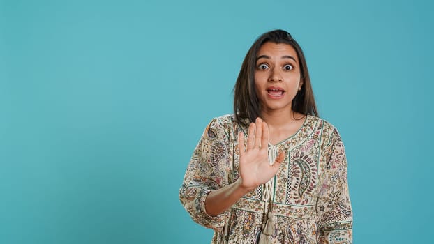 Stern indian woman doing stop hand gesture sign, complaining. Authoritative person doing firm halt sign gesturing, wishing to end concept, isolated over studio background, camera A