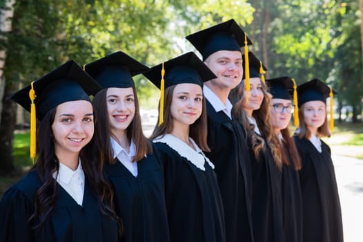 Row of happy young people in graduation gowns outdoors. Students in the park