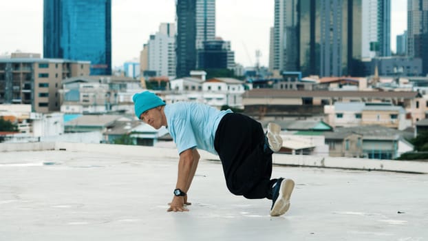 Skilled caucasian B-boy dancer practicing street dancing at rooftop with city sites or urban. Motion shot of young man performing street dance by doing freeze pose. Outdoor sport 2024. Endeavor.