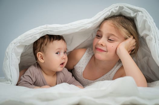 Little girl and her newborn brother hiding under the blanket