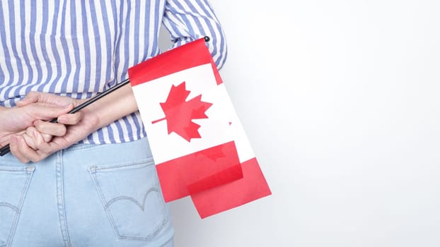 Unrecognized girl student in white blue shirt holding small Canadian flag over gray background, Canada day, holiday, vote, immigration, tax, copy space.