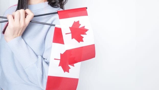 Unrecognized girl student in white blue shirt holding small Canadian flag over gray background, Canada day, holiday, vote, immigration, tax, copy space.