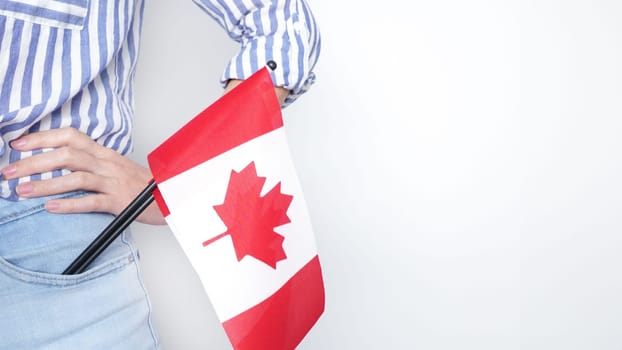 Unrecognized girl student in white blue shirt holding small Canadian flag over gray background, Canada day, holiday, vote, immigration, tax, copy space.