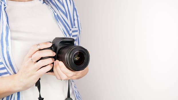 Photographer holding dslr camera. Self portrait, front view. Faceless nice woman with brown red hair in a tshirt with hands holding photo camera white background