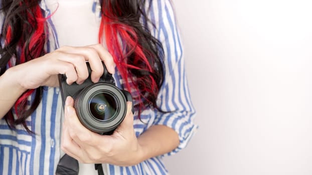 Photographer holding dslr camera. Self portrait, front view. Faceless nice woman with brown red hair in a tshirt with hands holding photo camera white background