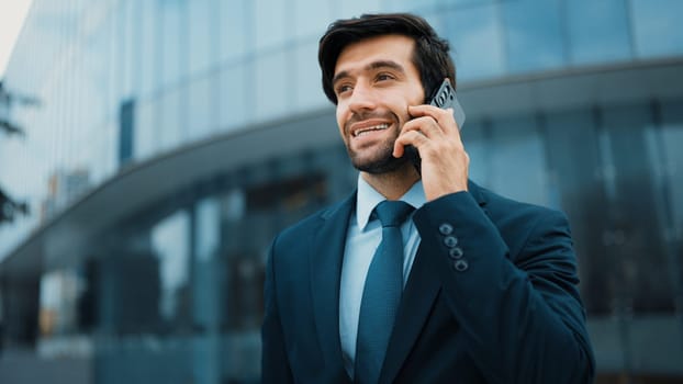 Skilled caucasian project manager calling phone while walking at city with blurred background. Skilled businessman using smart phone talking to project manager with blurred background. Exultant.