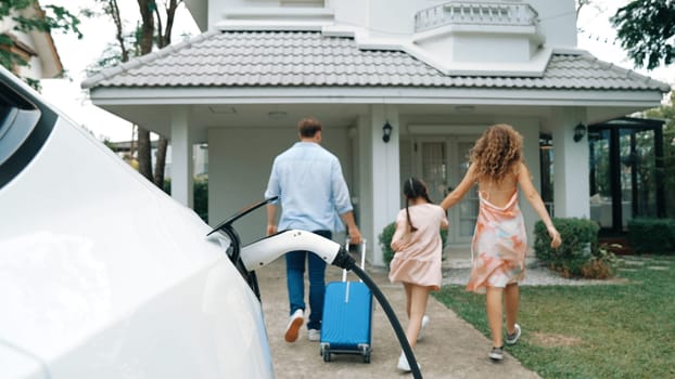 Happy family return from holiday and travel while recharging electric EV car's battery at home charging station. EV car and modern family concept. Synchronos