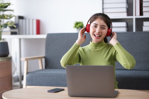 Young woman working on a laptop in a modern living room, wearing headphones, creating a comfortable and productive home office environment.