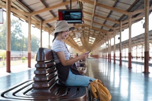 A young traveler sits at a train station with a backpack and smartphone, ready for an adventure. Perfect for travel, exploration, and journey-themed projects.