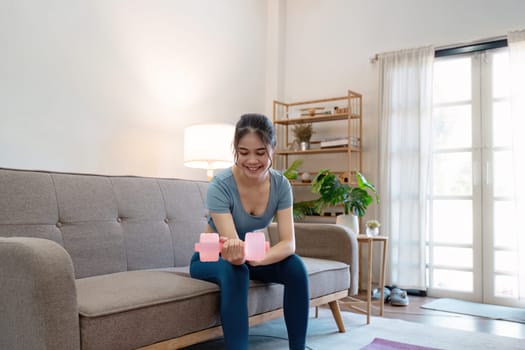 A young woman exercises with dumbbells in a cozy, modern living room, promoting a healthy lifestyle and home fitness.