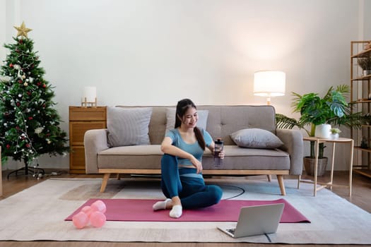 A young woman exercises at home on a yoga mat with dumbbells, surrounded by cozy modern furniture