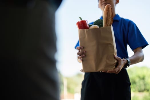 Close-up of a delivery person handing over a paper bag of groceries, symbolizing modern delivery services and convenience.