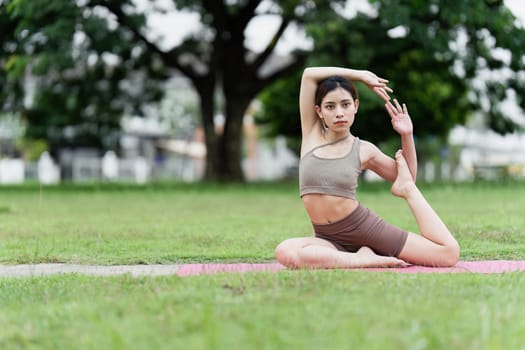 A young woman performing a yoga pose on a pink mat in a park, showcasing flexibility and balance, promoting health and wellness.