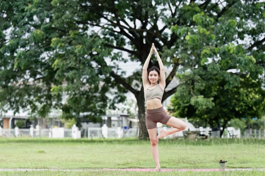 A young woman practicing yoga in a park, performing a tree pose, promoting wellness, mindfulness, and a healthy lifestyle.