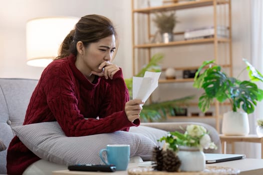 A young woman in a cozy living room setting, deeply focused on analyzing her bills and management her finances, representing modern banking and financial management.