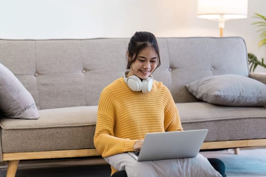 Young woman with headphones using a laptop in a cozy living room, embodying a relaxed and modern lifestyle.