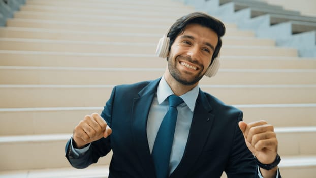 Closeup image of professional business man enjoy to listen music by using headphone. Portrait of skilled project manager show facial expression about joy and happy while sitting at mall. Exultant.