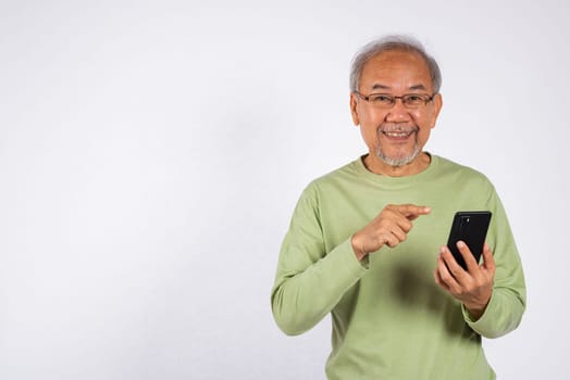 Portrait smiling Asian older man smiling and pointing at his cell phone studio shot isolated on white background. elderly holding mobile phone in hand. Concept of connection and communication