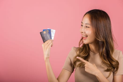 Portrait of Asian young woman holding bank card solution in hands in studio shot isolated on pink background, female smiling pointing and showing presenting credit card for online payment