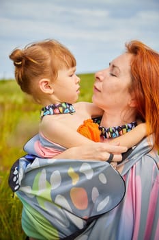 Happy female family with mother and daughter on green and yellow meadow full of grass and flower. Woman with red hair and blonde girl having fun, joy and hug in sunny summer day. Concept family love