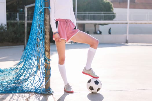 legs of an unrecognizable female football player stepping on a soccer ball next to the goal of an urban court, concept of sport and active lifestyle, copy space for text