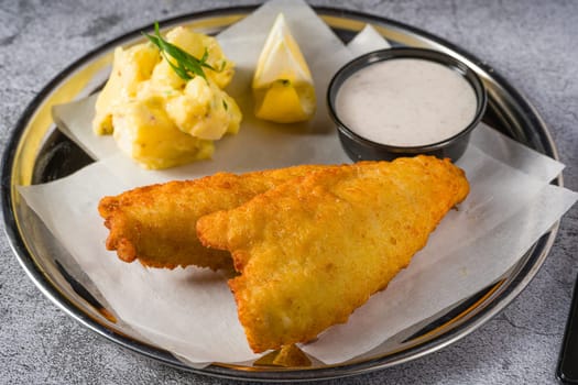 Deep fried coated fish fillet with potato salad on stone table