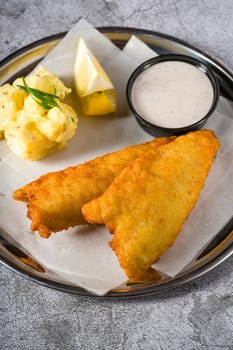 Deep fried coated fish fillet with potato salad on stone table