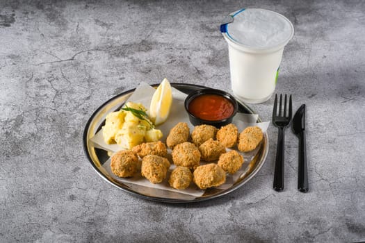 Fried mussels on a metal plate with potato salad on the side. Turkish name: Midye Tava