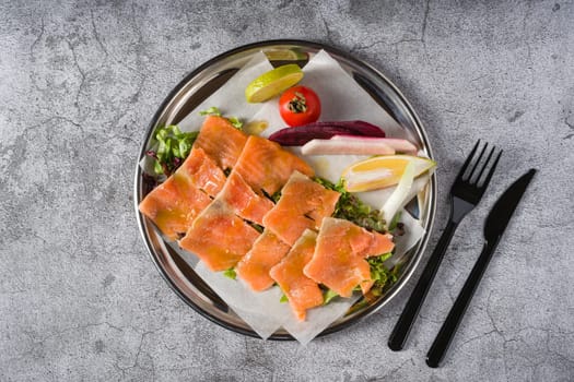Smoked salmon with greens under it on a stone table