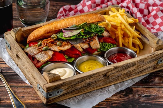 Steak sandwich with sauces and french fries on wooden table