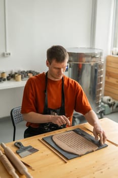 A potter cuts a piece of rolled clay with patterns. Vertical photo